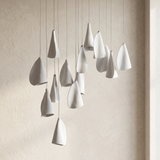 A modern multi-light pendant chandelier with teardrop-shaped white ceramic shades hanging from thin cables against a textured beige wall.