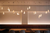 White porcelain chandelier shades hang at staggered heights above wooden dining tables and dark seating in a softly lit interior.