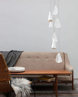 White porcelain chandelier with folded shades hanging at staggered heights beside a beige sofa and wooden coffee table.