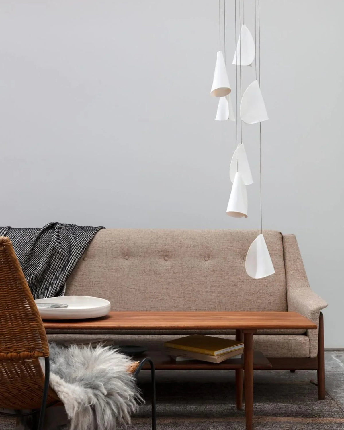 White porcelain chandelier with folded shades hanging at staggered heights beside a beige sofa and wooden coffee table.