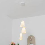 A three-light white porcelain chandelier hangs from a round ceiling canopy in a white room with flowers and wall decor.