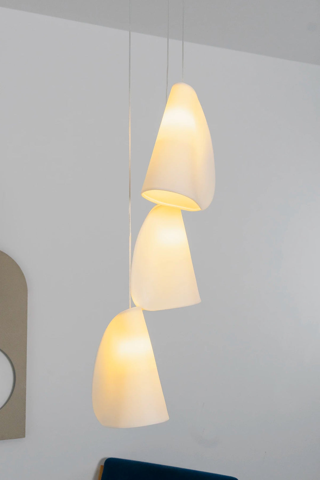 A chandelier with three glowing white porcelain shades hangs at staggered heights against a white wall above dark seating.