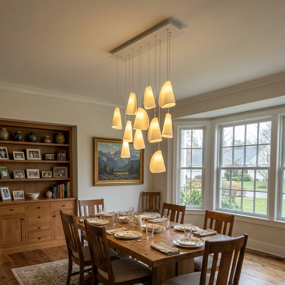 A modern multi-light linear chandelier with ten warm white cone-shaped pendant lights hanging over a wooden dining table set for a meal in a bright, traditional dining room.