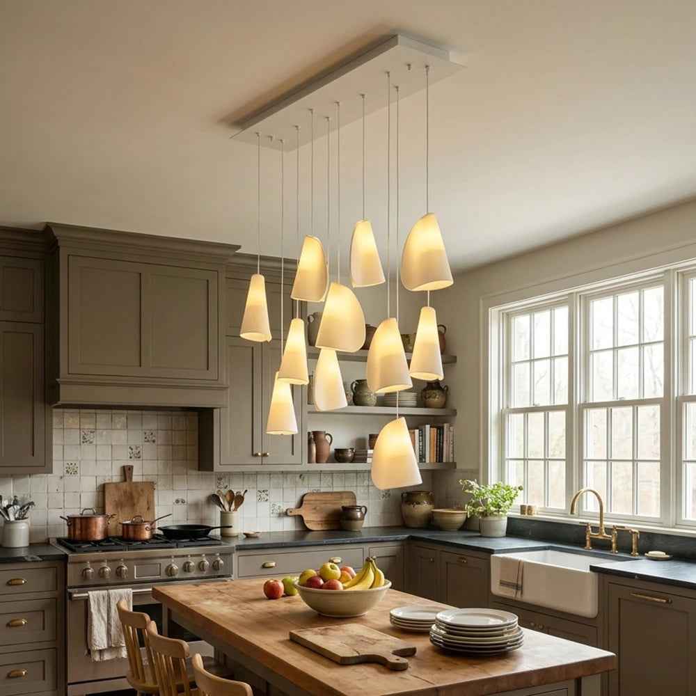 A modern multi-light linear pendant chandelier with ten warm white tapered glass shades hanging over a wooden kitchen island in a styled kitchen setting.