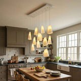 A modern multi-light linear pendant chandelier with ten warm white tapered glass shades hanging over a wooden kitchen island in a styled kitchen setting.