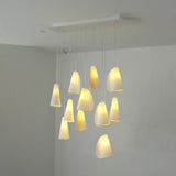 A modern multi-light pendant chandelier with multiple white fabric shades of varying shapes and sizes, suspended from a white ceiling plate in a minimalist room.