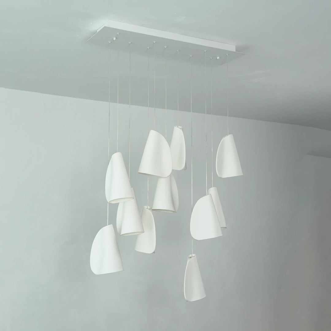 White porcelain chandelier viewed at an angle, with folded shades hanging at different heights beneath a rectangular canopy in a white room.