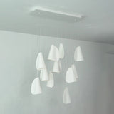 White porcelain chandelier viewed at an angle, with folded shades hanging at different heights beneath a rectangular canopy in a white room.