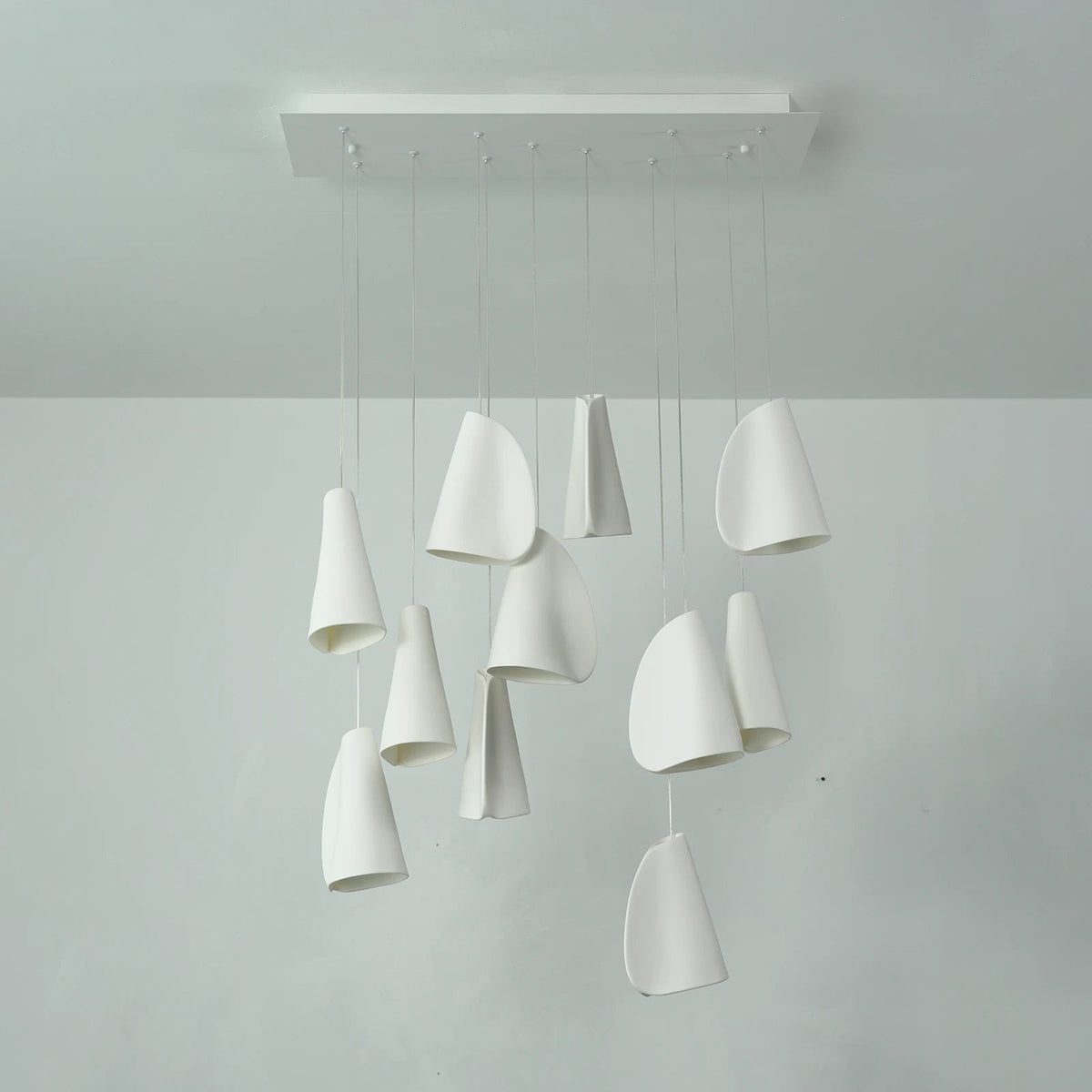 White porcelain chandelier with folded shades suspended at varied heights from a rectangular ceiling canopy, viewed from the front.