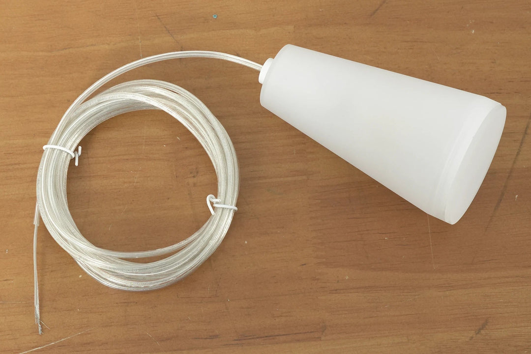 A white porcelain chandelier shade rests beside its coiled clear cable on a wooden surface.