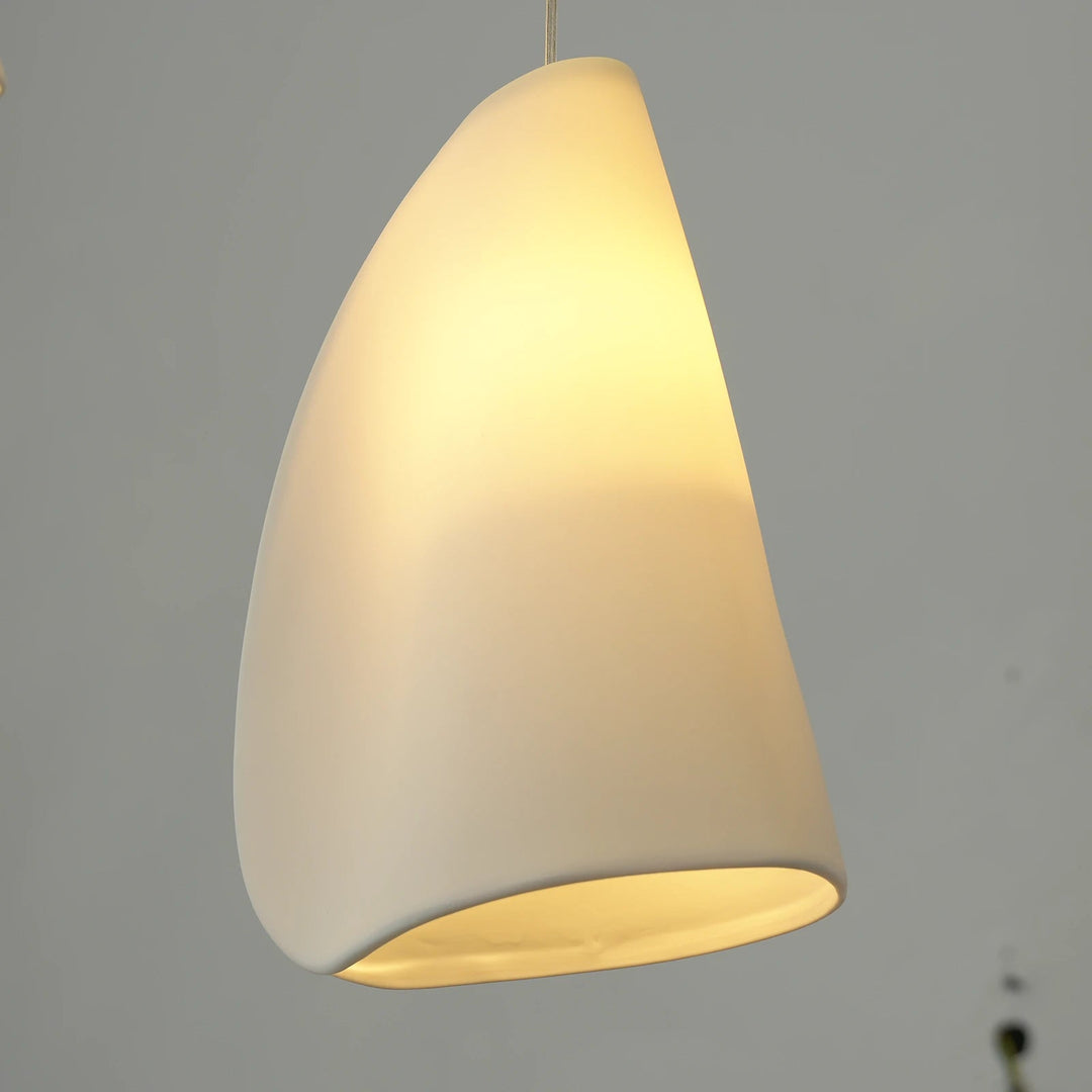 A chandelier shade in folded white porcelain glows yellow against a gray background.
