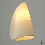 A chandelier shade in folded white porcelain glows yellow against a gray background.