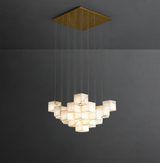 A modern multi-light pendant chandelier with a square gold-toned ceiling canopy and multiple illuminated white marble cube shades suspended by thin cables against a dark gray wall.