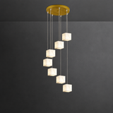 A modern multi-light linear pendant chandelier with a gold circular ceiling canopy and six cascading square marble-look glass shades, shown against a dark gray wall.