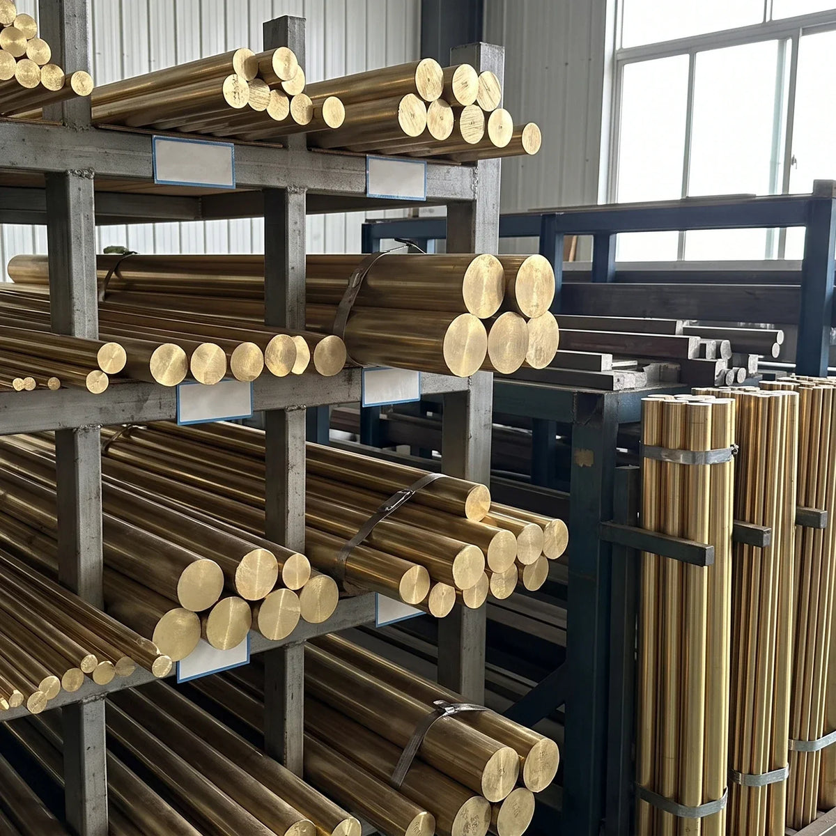 Bundles of brass rods stacked horizontally and vertically on workshop racks, with no chandelier visible.