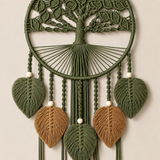 A macrame wall hanging featuring a tree of life design in olive green, with five hanging leaf-shaped tassels in olive green and two larger leaf tassels in tan, accented by small white beads.