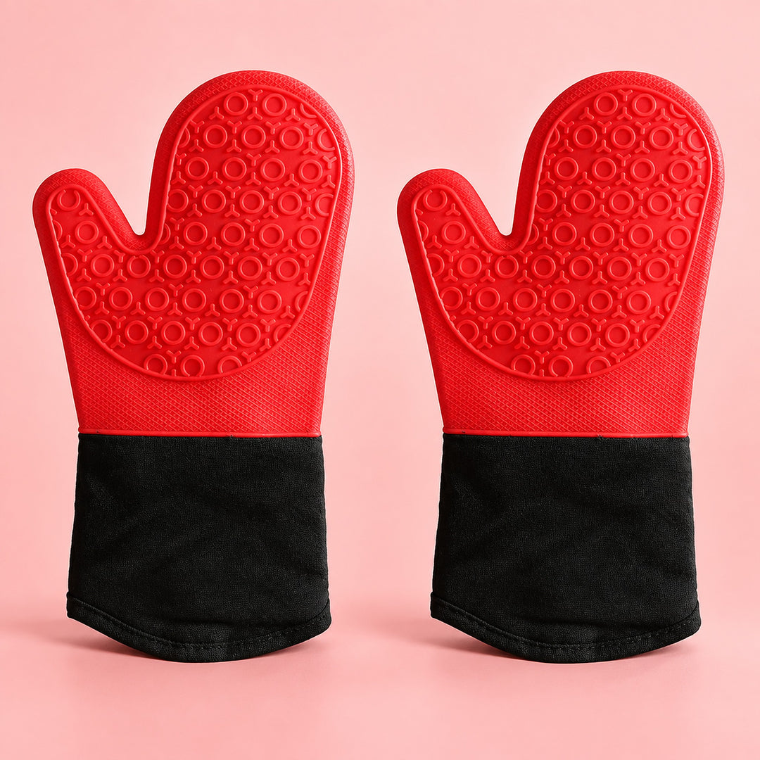 A pair of silicone oven mitts with textured red palms and black cuffs, displayed side-by-side on a solid pink background.