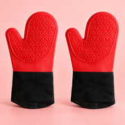 A pair of silicone oven mitts with textured red palms and black cuffs, displayed side-by-side on a solid pink background.