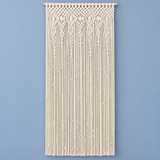 An off-white macrame wall hanging with intricate woven geometric patterns at the top and long hanging cords below, displayed against a solid light blue background.