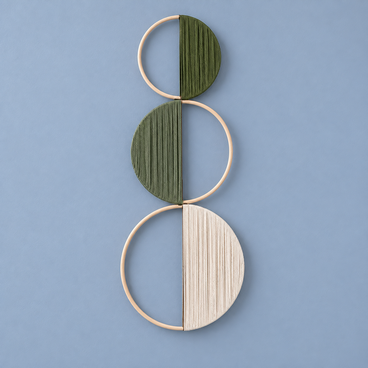 Olive green and cream yarn wound across three stacked wooden hoops on a dusty blue wall