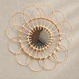 A circular woven rattan wall mirror with a sunburst frame design, mounted on a neutral beige wall.