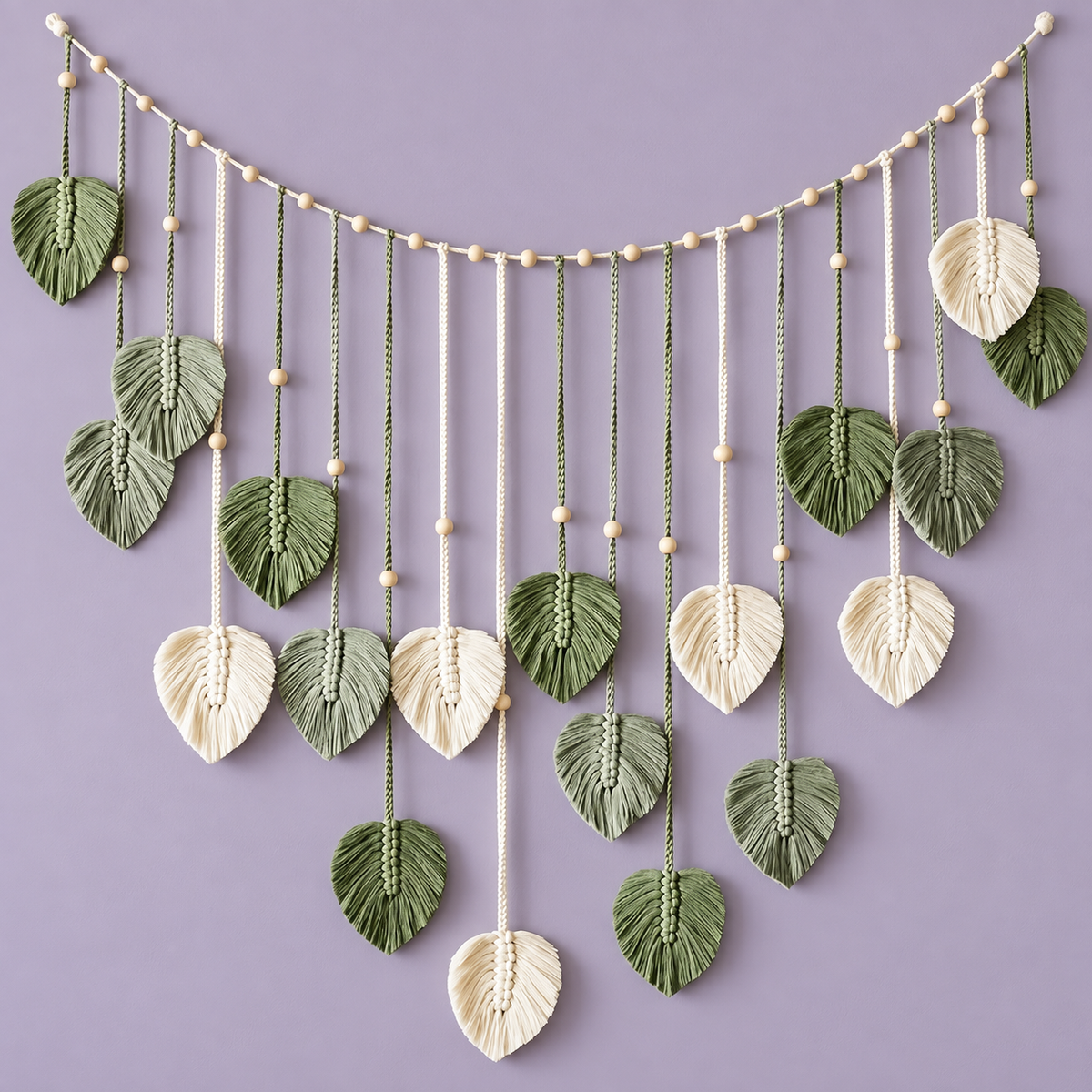 Sage and cream macrame leaves hanging from a beaded swag cord on a lilac wall