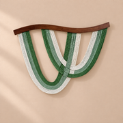 Deep green and cream rope arcs under a curved dark batten on a sand wall