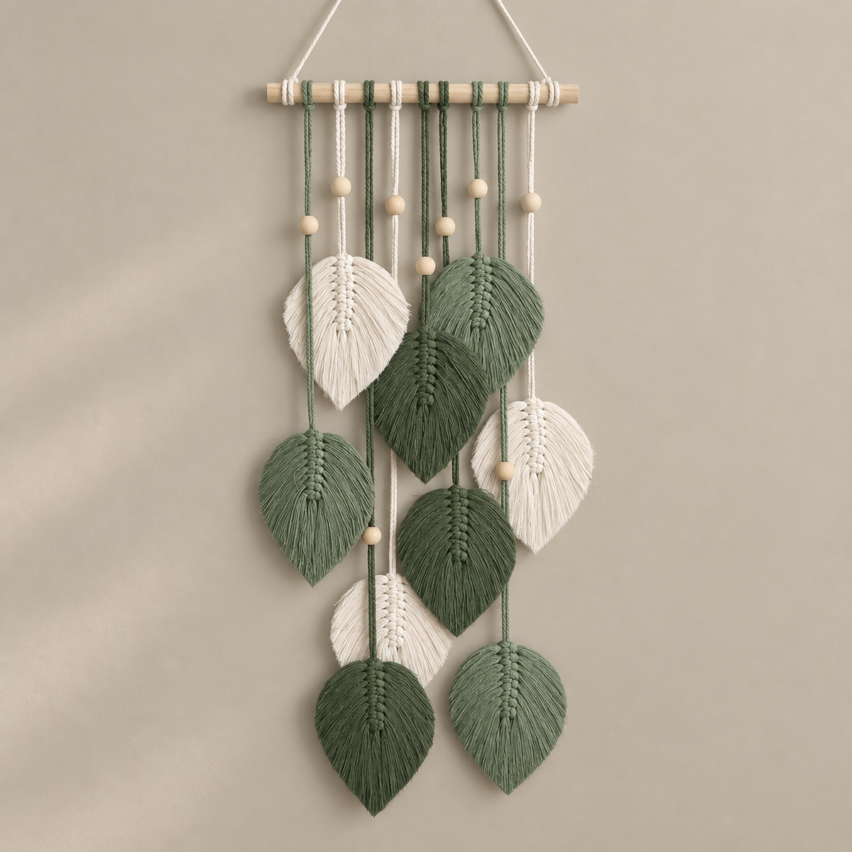 Green studio on cream, macrame leaf cascade on a dowel, twisted cord, combed flat at the leaves, pale wooden dowel