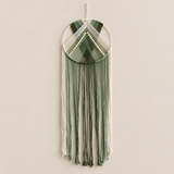 A bohemian-style woven wall hanging macrame dreamcatcher with sage green and cream cord, hanging on a neutral beige wall.