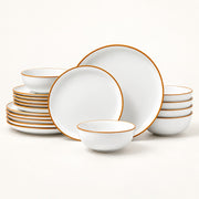 White ceramic dinnerware set with a thin gold rim, including plates, bowls, and stacked serving pieces, photographed on a clean white background.