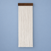 Cream straight cord fringe wall hanging on a dark wood batten against a blue wall
