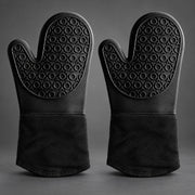 A pair of black silicone oven mitts with textured non-slip grips and a fabric cuff, displayed side-by-side on a dark gray background.