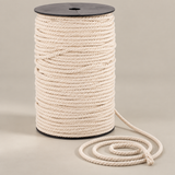A large spool of thick, cream-colored twisted cotton rope with a black plastic top and bottom, shown on a neutral beige background with a short section of the rope coiled in front.