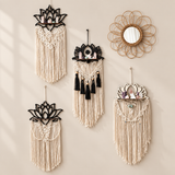 Four bohemian-style wall hangings and one round woven mirror arranged on a beige wall. The set includes cream macrame fringe, black lotus-shaped metal cutouts, and a natural tan woven sunburst frame.