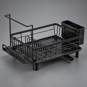 A black metal dish rack with a draining tray, a vertical drying handle, and a side cup holder, photographed on a neutral gray studio background.