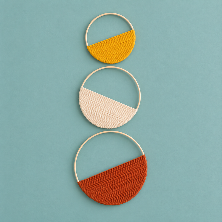 Mustard, cream and rust yarn half filling three wooden hoops stacked on a pale teal wall