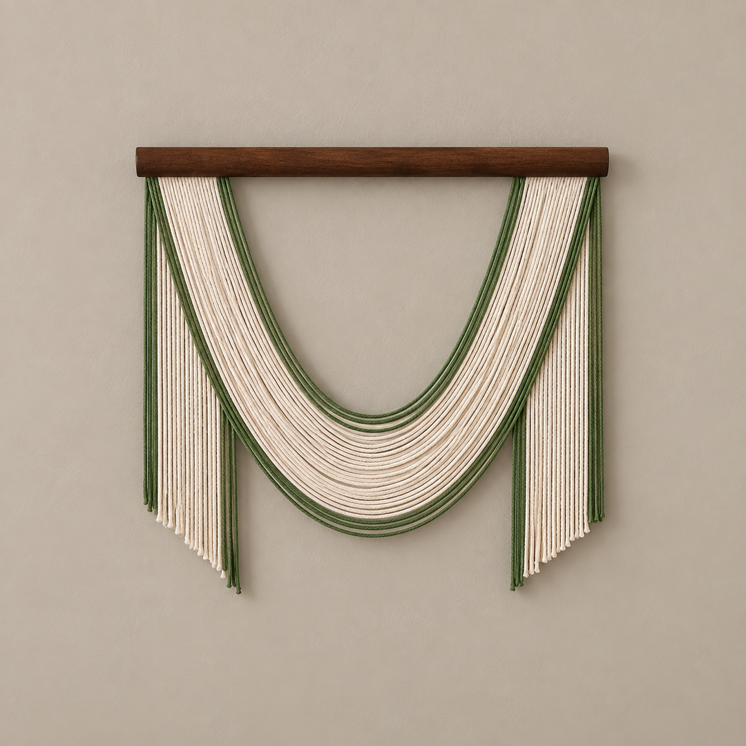 A bohemian-style macrame wall hanging with a dark brown wooden dowel, featuring cream-colored cords and green stripes arranged in a U-shape with fringe details, mounted on a neutral beige wall.