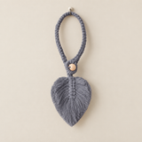 A gray macrame leaf-shaped hanging ornament with a braided loop and a small wooden bead accent, shown against a plain beige background.