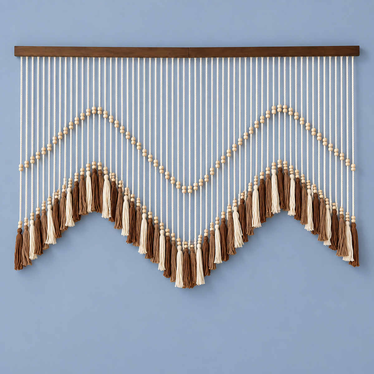 A bohemian-style wall hanging macrame wall decor with a dark wood top bar, cream and brown cord strands, and tassel accents, displayed against a solid light blue wall.