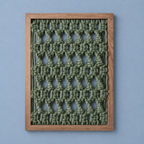 A square framed wall art piece featuring an olive green knotted textile pattern in a wooden frame, set against a solid light blue background.
