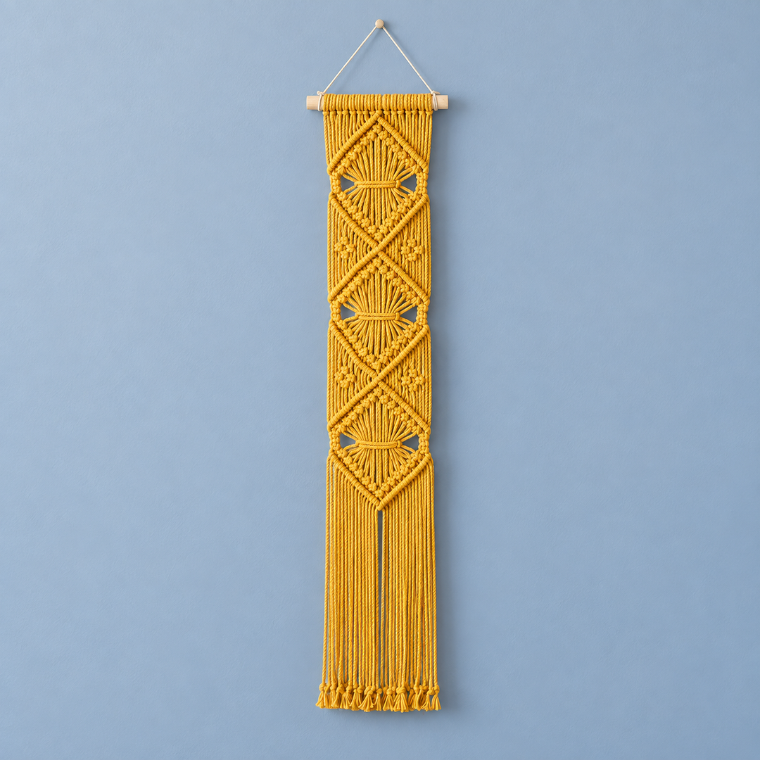 A yellow macrame wall hanging with geometric woven patterns and a hanging string, suspended from a wooden dowel against a light blue wall.