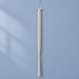 A long cream macrame wall hanging suspended from a light wood dowel, displayed against a soft blue wall with subtle shadow patterns.