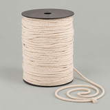 A spool of thick, cream-colored twisted cotton rope with a black plastic core, shown on a neutral light gray background with a length of the rope coiled in front.