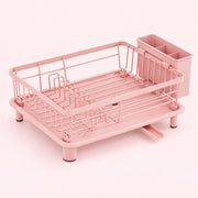 A pink metal and plastic dish rack with a matching cup holder, shown on a solid pale pink background.
