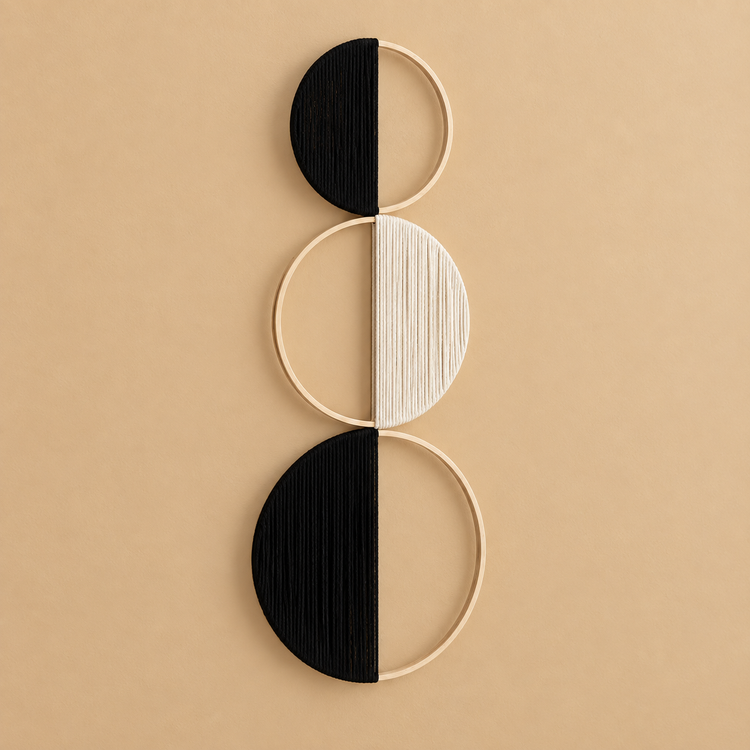 Black and cream yarn wound across three stacked wooden hoops on a sand colored wall