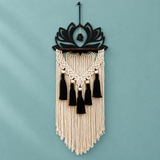 Black laser cut lotus above a wooden ledge with black tassels on a teal wall