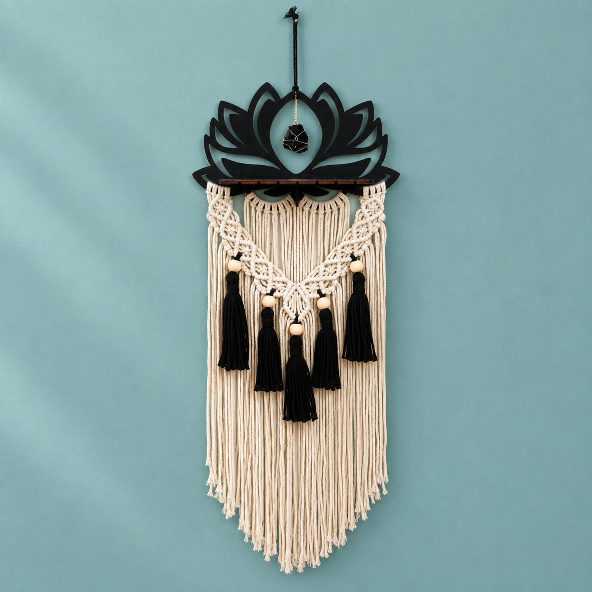 Black laser cut lotus above a wooden ledge with black tassels on a teal wall