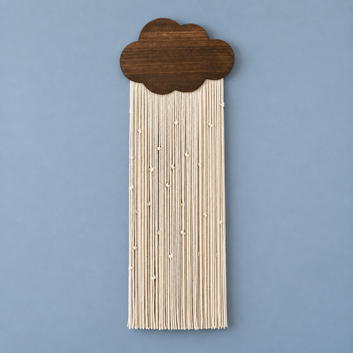 A cloud-shaped wall hanging with a dark brown wood top and cream-colored string fringe, shown against a solid blue background.