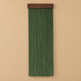 A vertical green macrame wall hanging with a dark brown wooden top bar, displayed against a solid beige background.