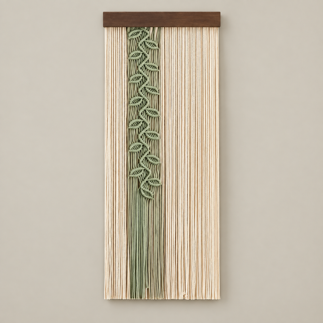 A vertical woven wall hanging with a natural wood top bar, featuring a central sage green leafy vine pattern over a background of vertical beige and light brown fibers, shown against a neutral beige wall.
